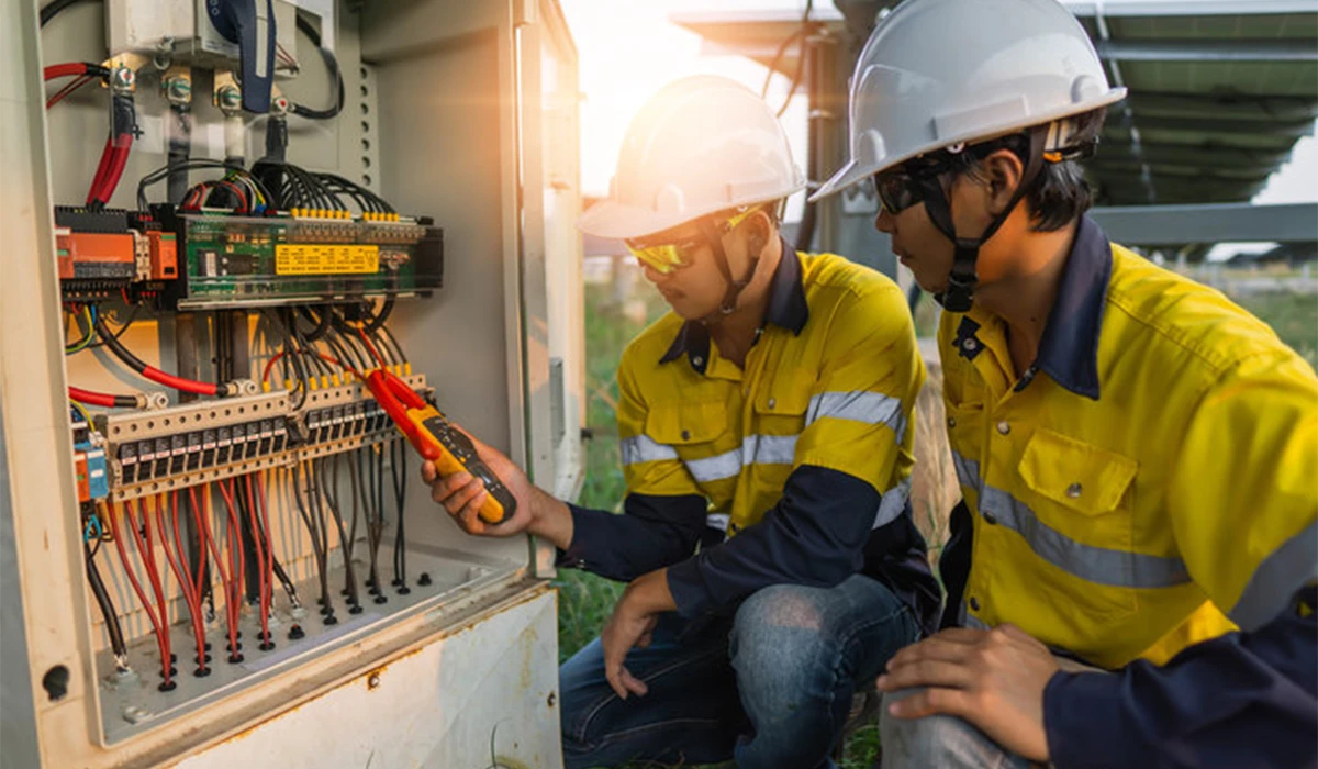 Electricians performing electrical services while inspecting and testing an industrial control panel with safety gear in an outdoor setting 